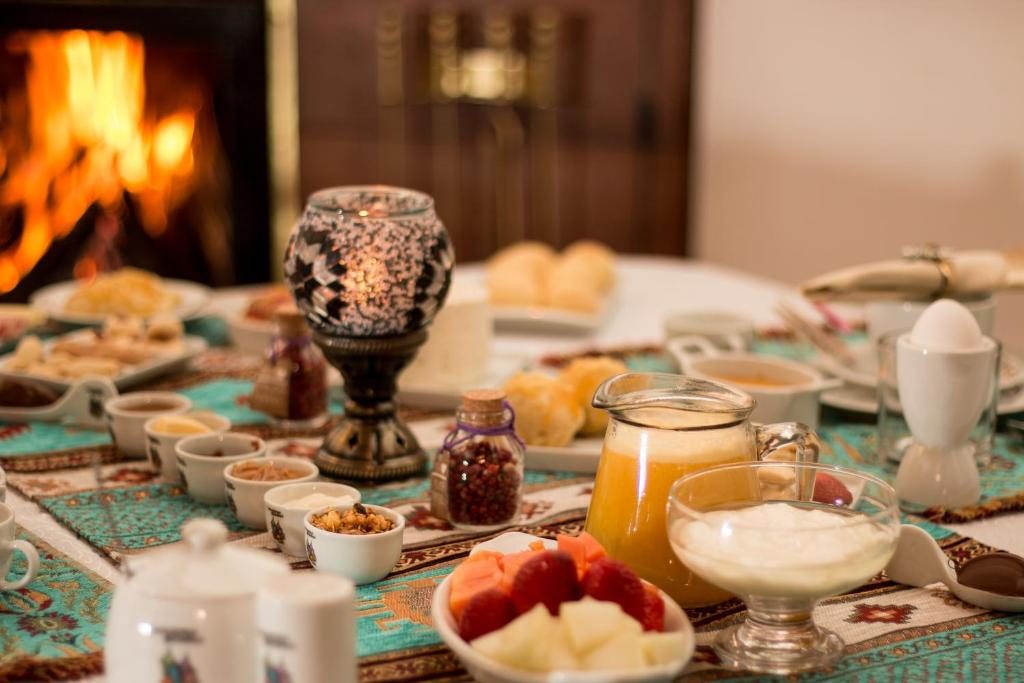 Mesa do café da manhã com frutas, cereais, suco e vela acesa diante da lareira
